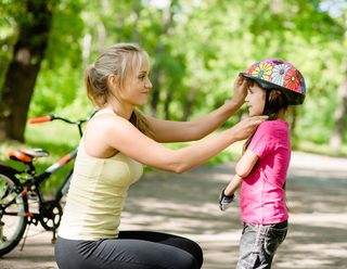 A mom adjusts her daughter's bike helmet.