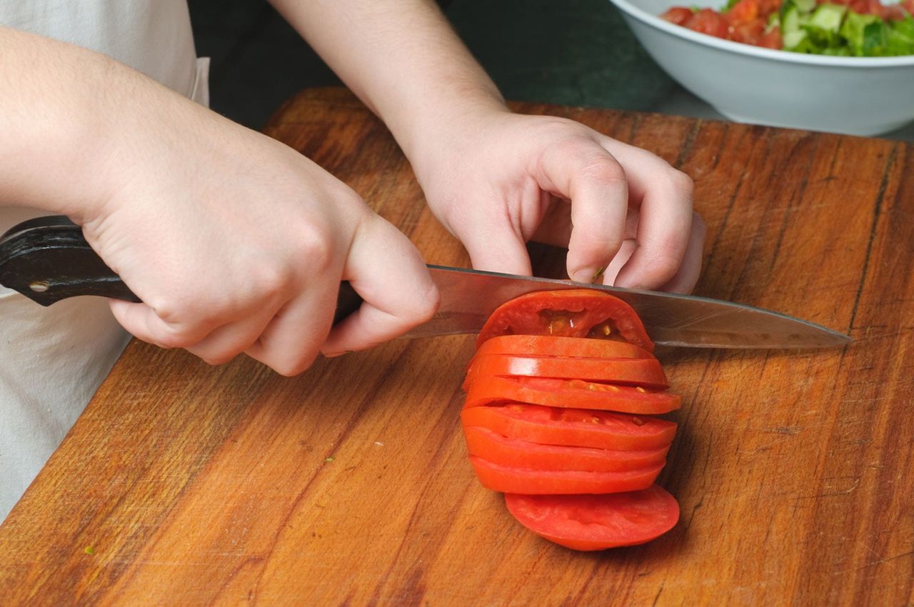 Person Slicing Tomatoes On A Wooden Cutting Board