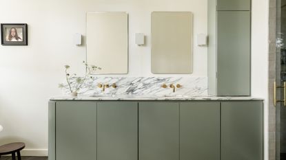 A minimalist, modern bathroom with a muted green vanity, off-white walls, double sinks with marble countertops and two rectangular mirrors on the wall.
