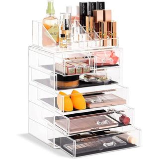 A clear, tall makeup organizer features six drawers and a large compartment above