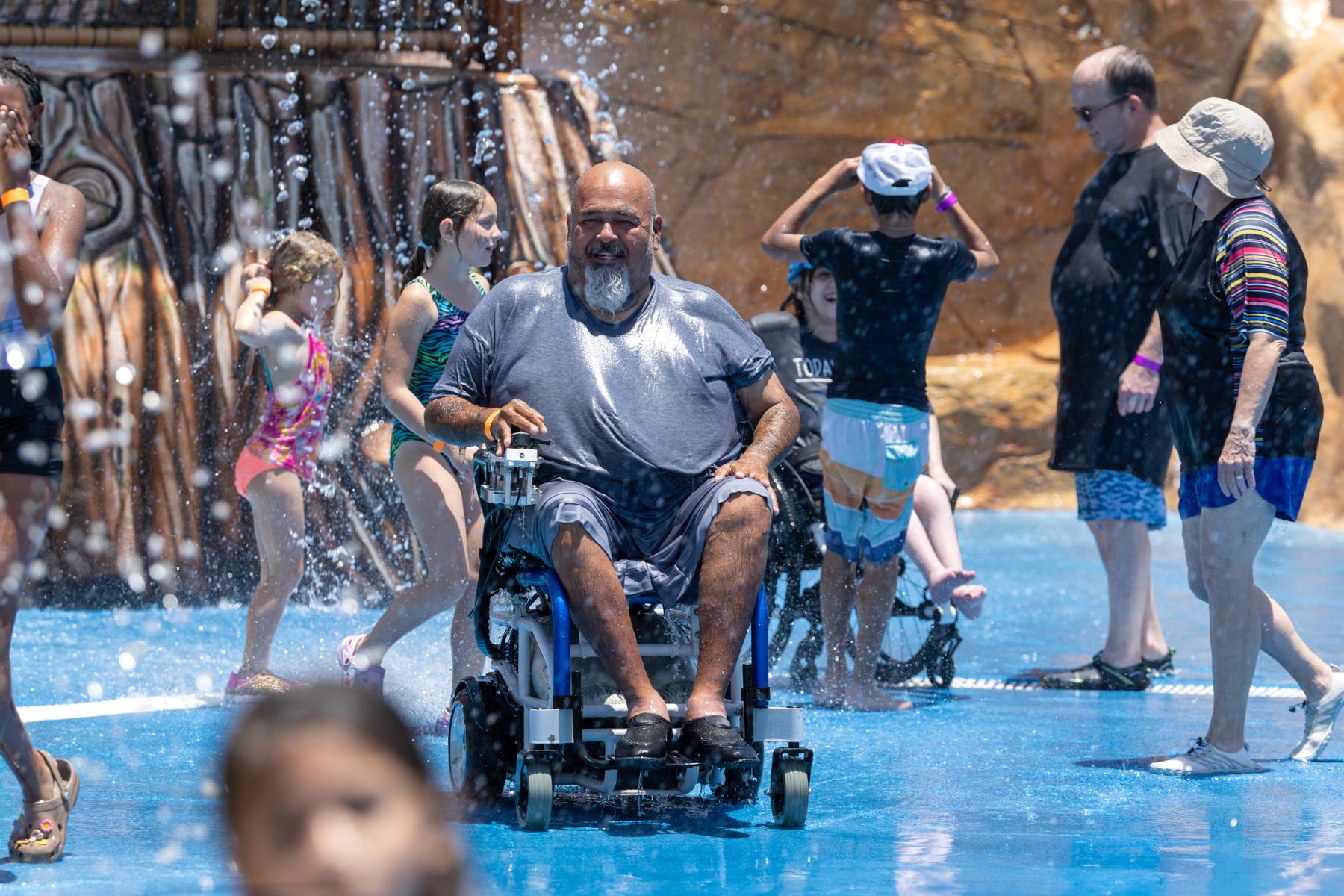 A man in a wheelchair uses a splash pad at Morgan's Inspiration Island