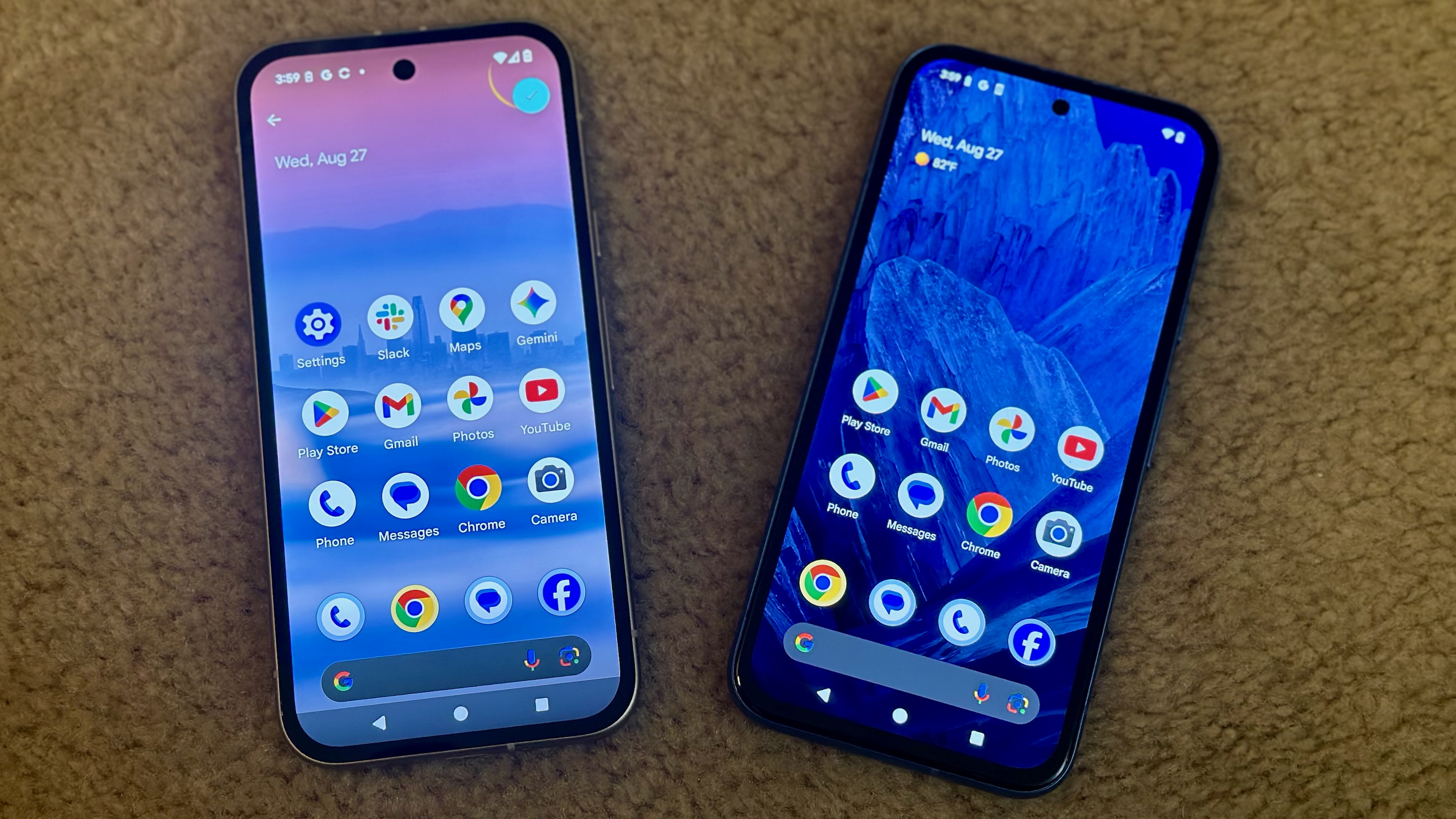 The Google Pixel 9a (left) and Google Pixel 8a (right) laying on carpet face-up, showing the 9a's brighter, slightly larger AMOLED display compared to the 8a's.