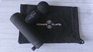 Power Plate Mini+ massage gun with attachment, lying on carry bag