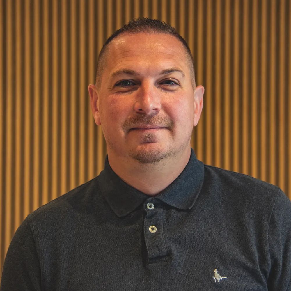 Headshot of a man standing in front of a slatted wood wall