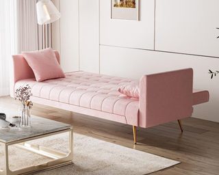 A pastel pink sofa bed in a living room next to a table with a vase of flowers on it