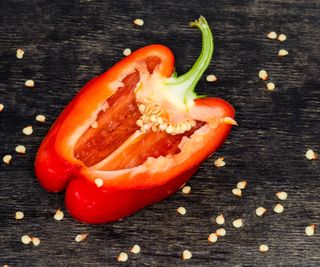 Red bell pepper cut in half with seeds scattered about a wood table.