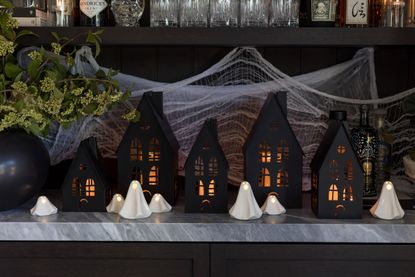 A Halloween scenescape with black cardboard houses and white ceramic ghost decorations