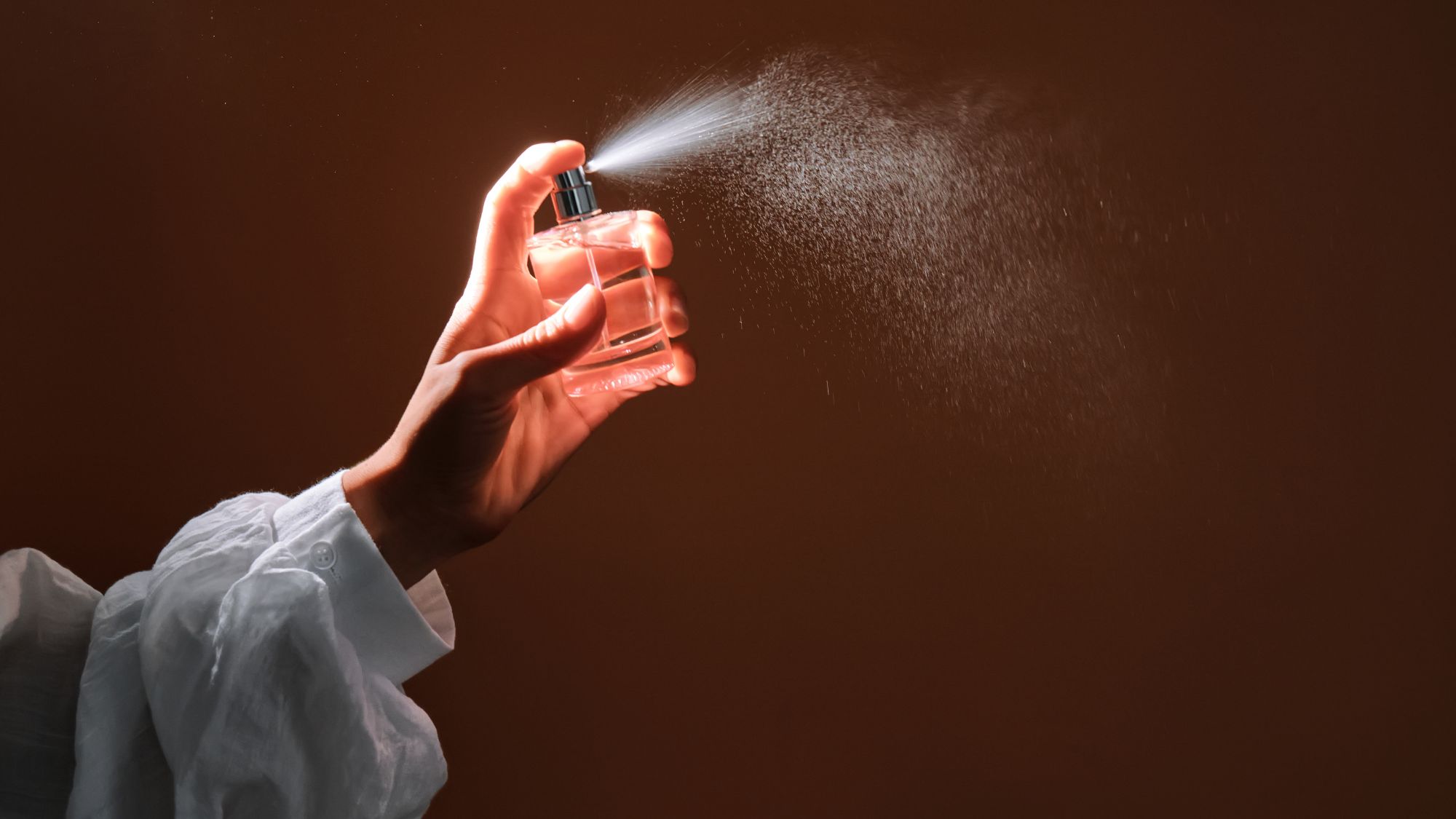 a close up of a woman&#039;s arm in a white loose-fit blouse spraying a room spray into the air