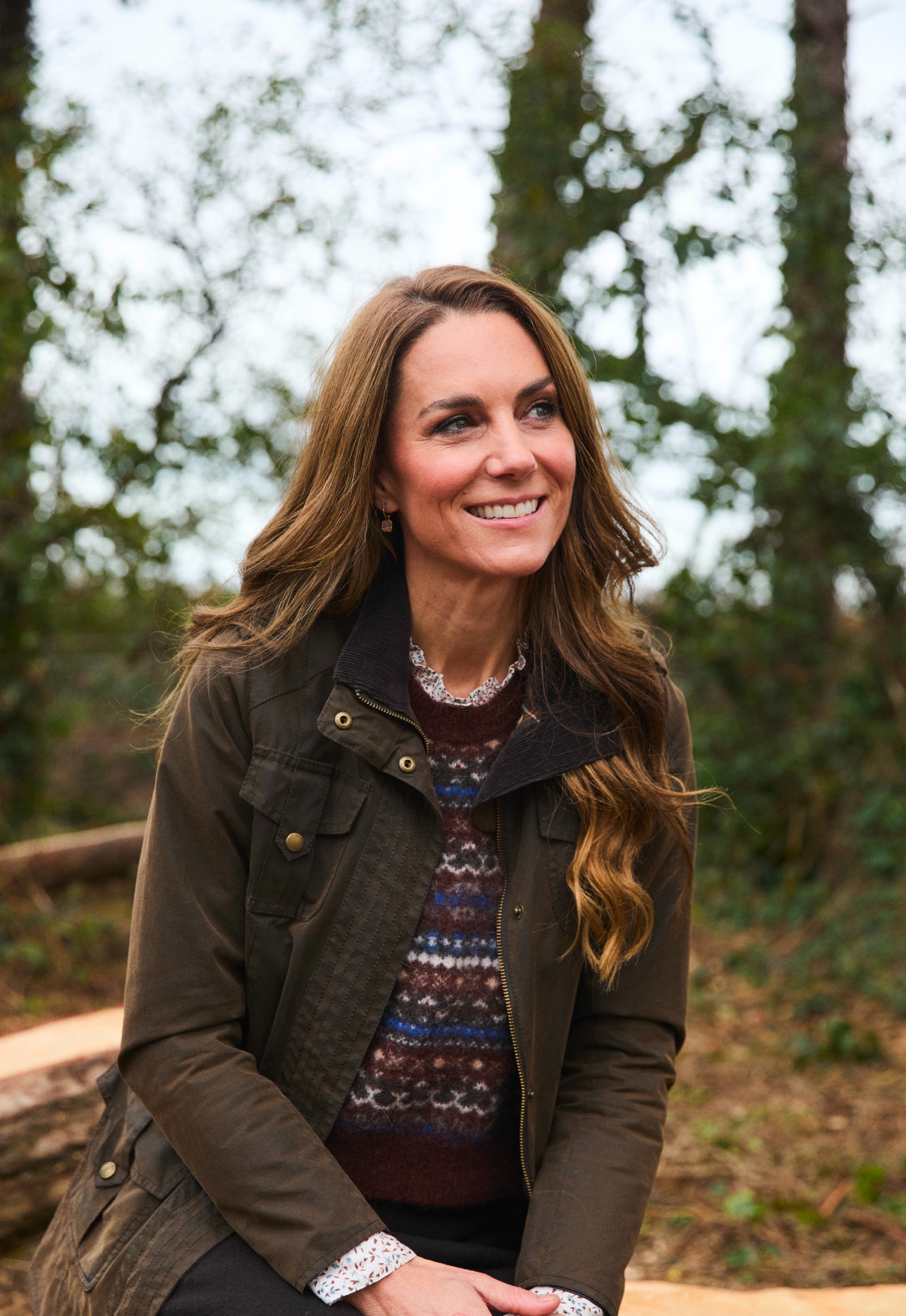 Princess Kate wearing a sweater and coat smiling in front of trees