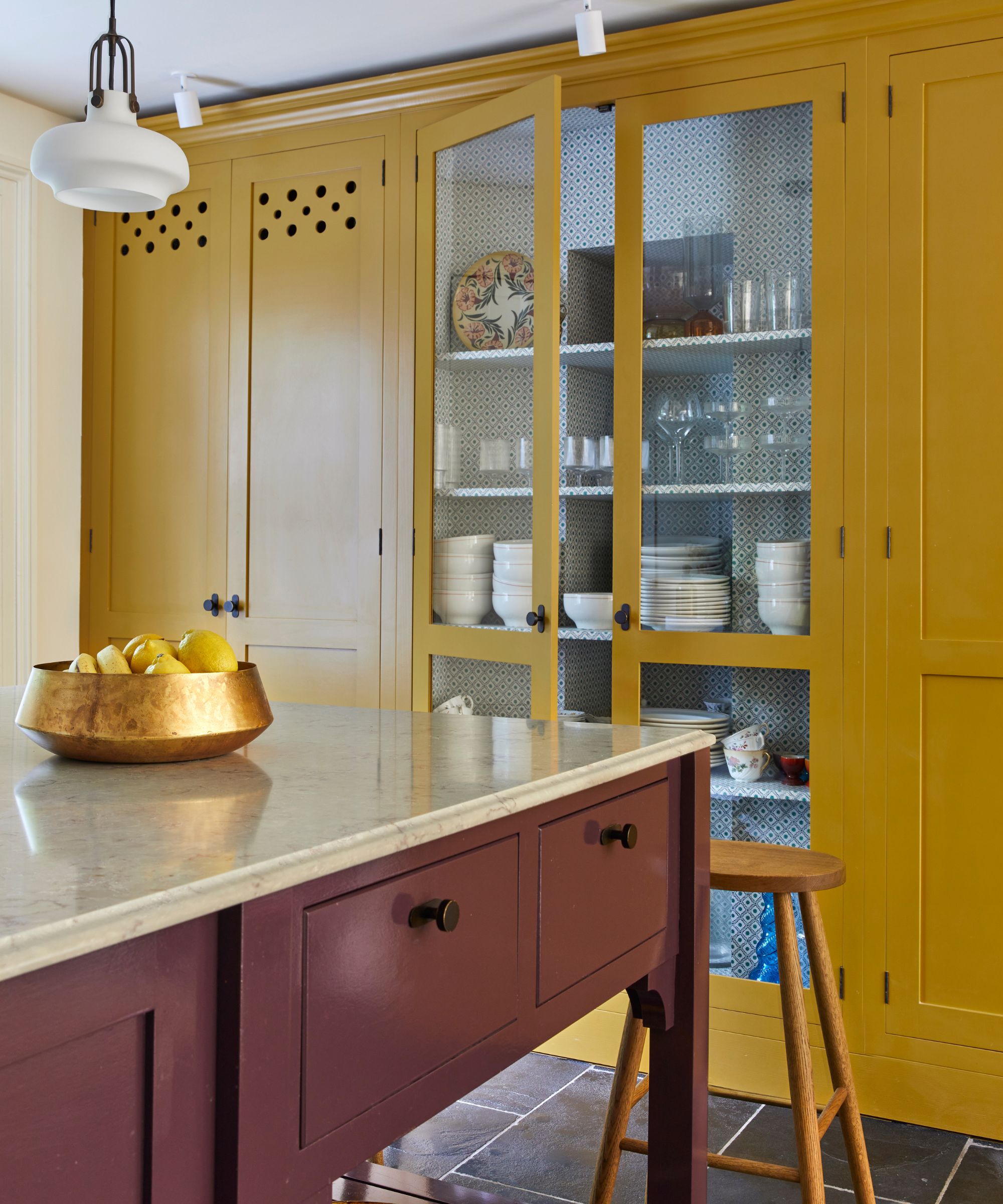 Kitchen with slate floor, red kitchen island, yellow cabinets with plates, glassware and bowls
