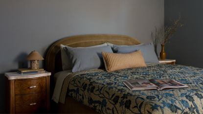 A beautiful blue bedroom with a wood side table a small table lamp. blue pillows, a striped bolster, a patterned quilt, and a curved green headboard