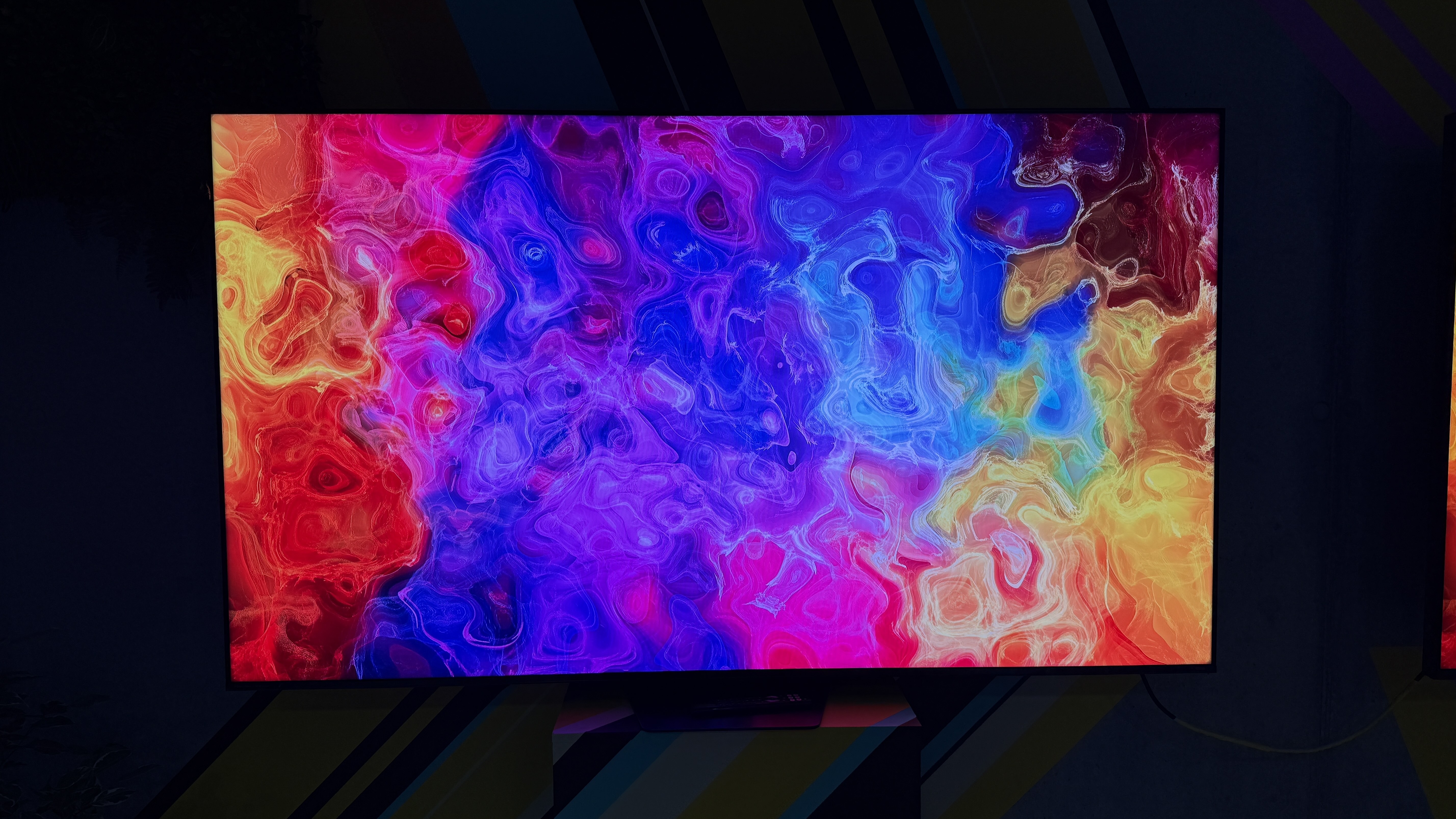 The Hisense UR9S RGB TV in a dark room, with a pattern of rippling colors on the screen showing its impressive color reproduction