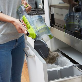Person emptying a Black + Decker vacuum cleaner dust bag into bin.