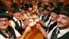 Several men in lederhosen hold up beer steins 