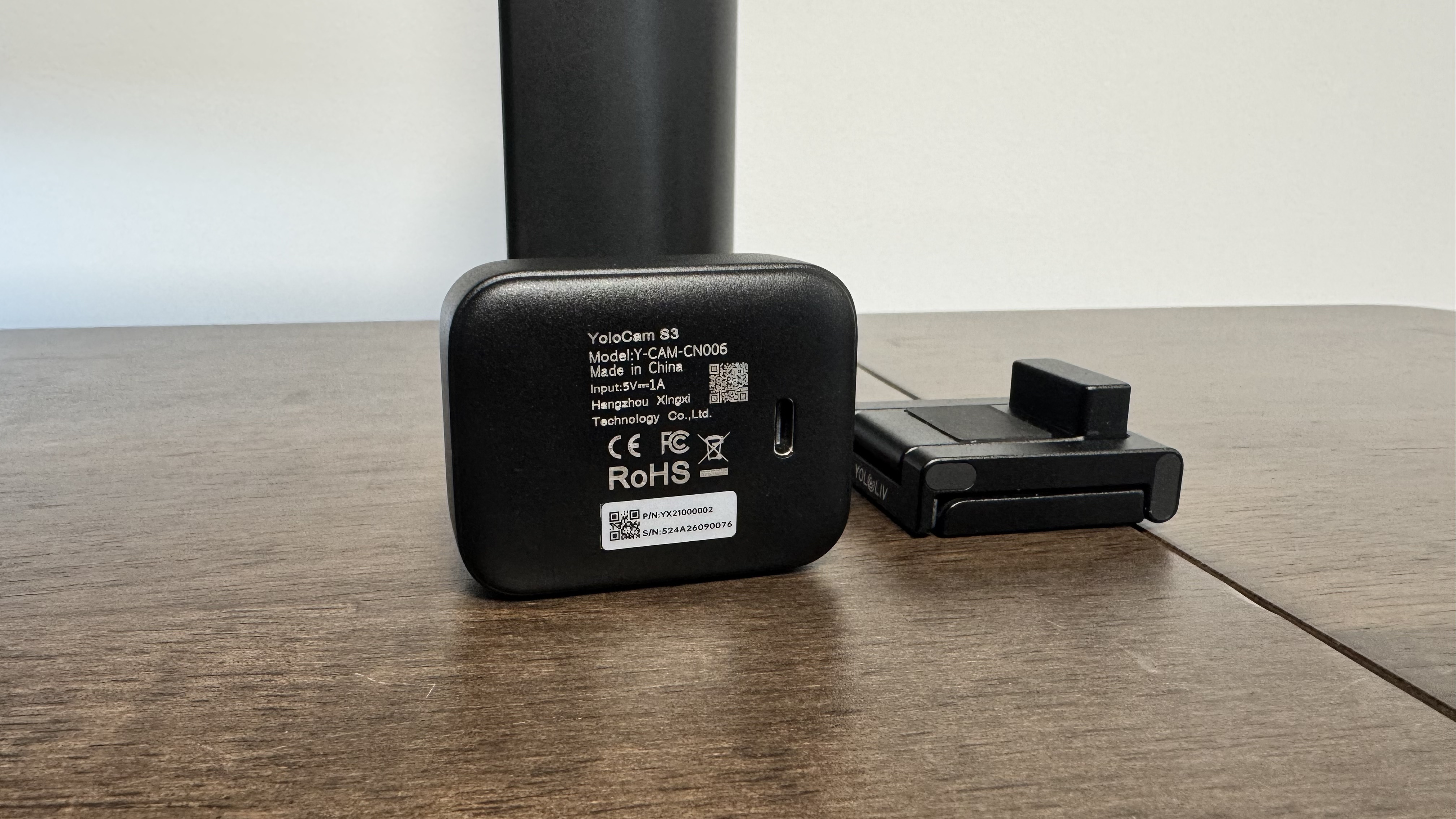 The Yololiv YoloCam S3 4K webcam from the back on a wooden table, next to its stand