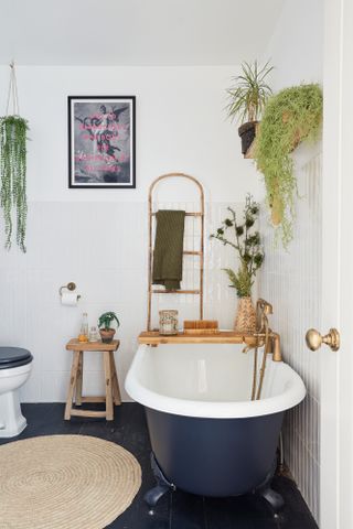 Bathroom with white tiled walls, black painted wooden floor, dark blue roll-top bath, jute rug and wooden accessories