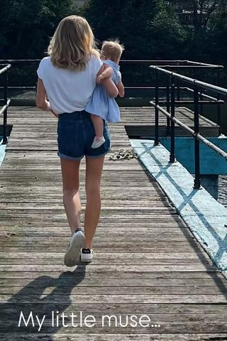 Chelsy Davy in jean shorts and a white t-shirt walking on a boardwalk carrying a baby