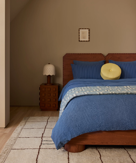 a bedroom with blue bedding, a round yellow pillow, a dark wood bedframe and side table, and a small accent lamp