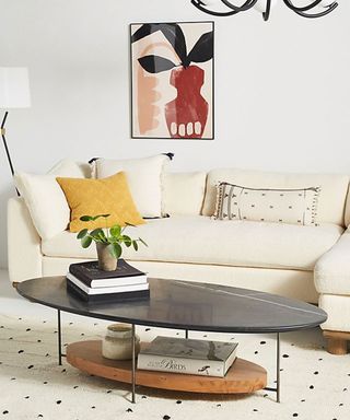 Modern and playful living room with ellipse shape, two-tier coffee table, boucle white sofa and framed abstract print on wall