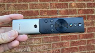 Xgimi Aura 2 home cinema projector remote control held in hand against brick wall