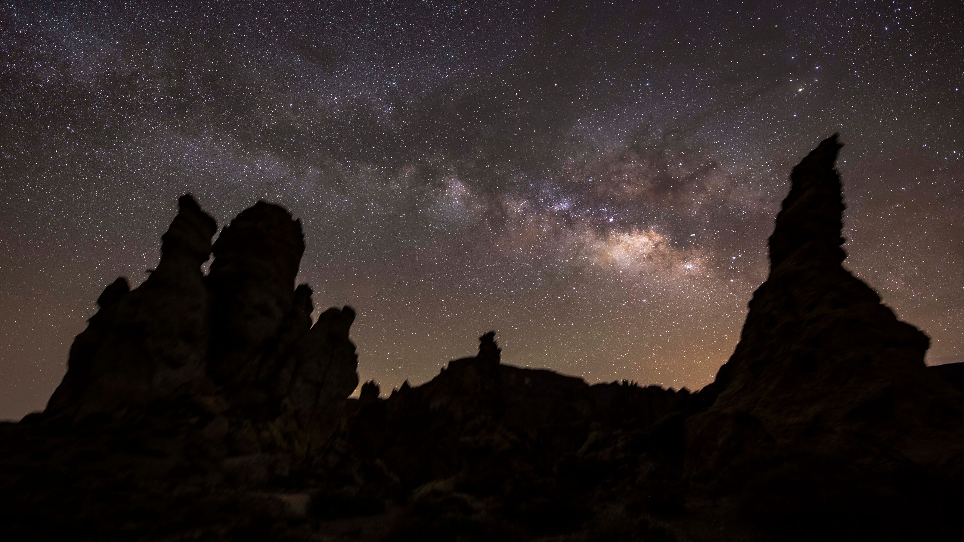 A photo of the a rocky landscape set against the galactic core of the Milky Way in the sky above.