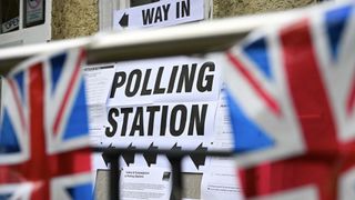 A photo of a polling station sign placed on a wall between two blurred flags of the United Kingdom