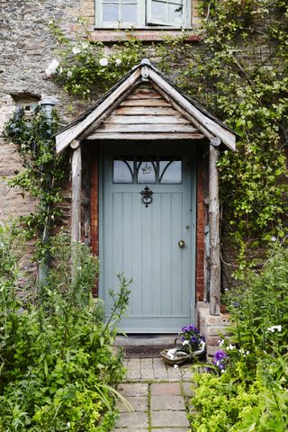 A blue front door on a cottage with ivy climbing up the porch