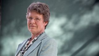 Jocelyn Bell Burnell smiles toward the camera while wearing a gray suit and a patterned shirt.