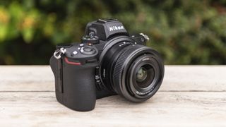 Nikon Z5 set skråt forfra på et tråbord med grønne buske i baggrunden