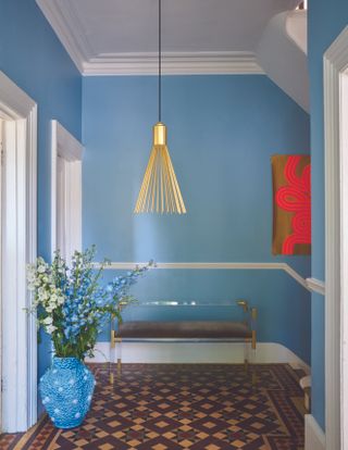 sky blue entryway with artwork, tiled floor, pendant light, bench