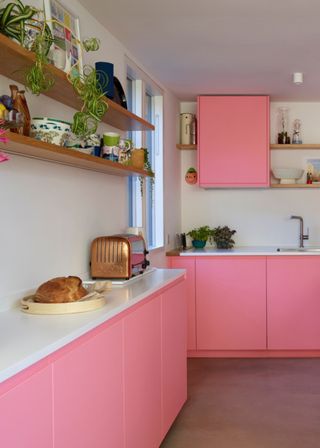 A kitchen with bright pink kitchen cabinets and white countertops