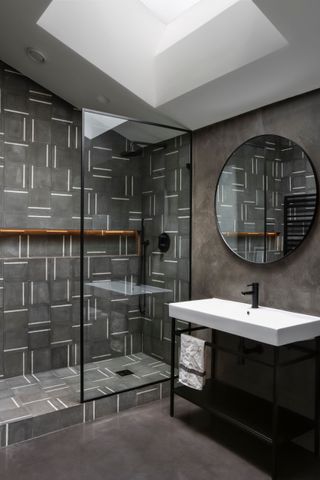 Dark floors, walls and shower tiles with white sink and ceiling and skylight