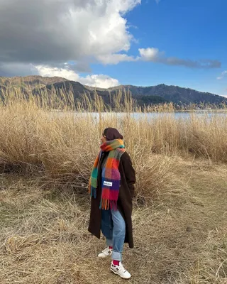 Yusra wears a brown long coat, plaid scarf, blue cuff jeans, red socks, and white new balance sneakers.