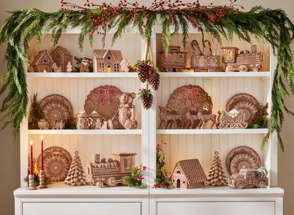 a dresser filled with ceramic gingerbread christmas decor with a garland draped above