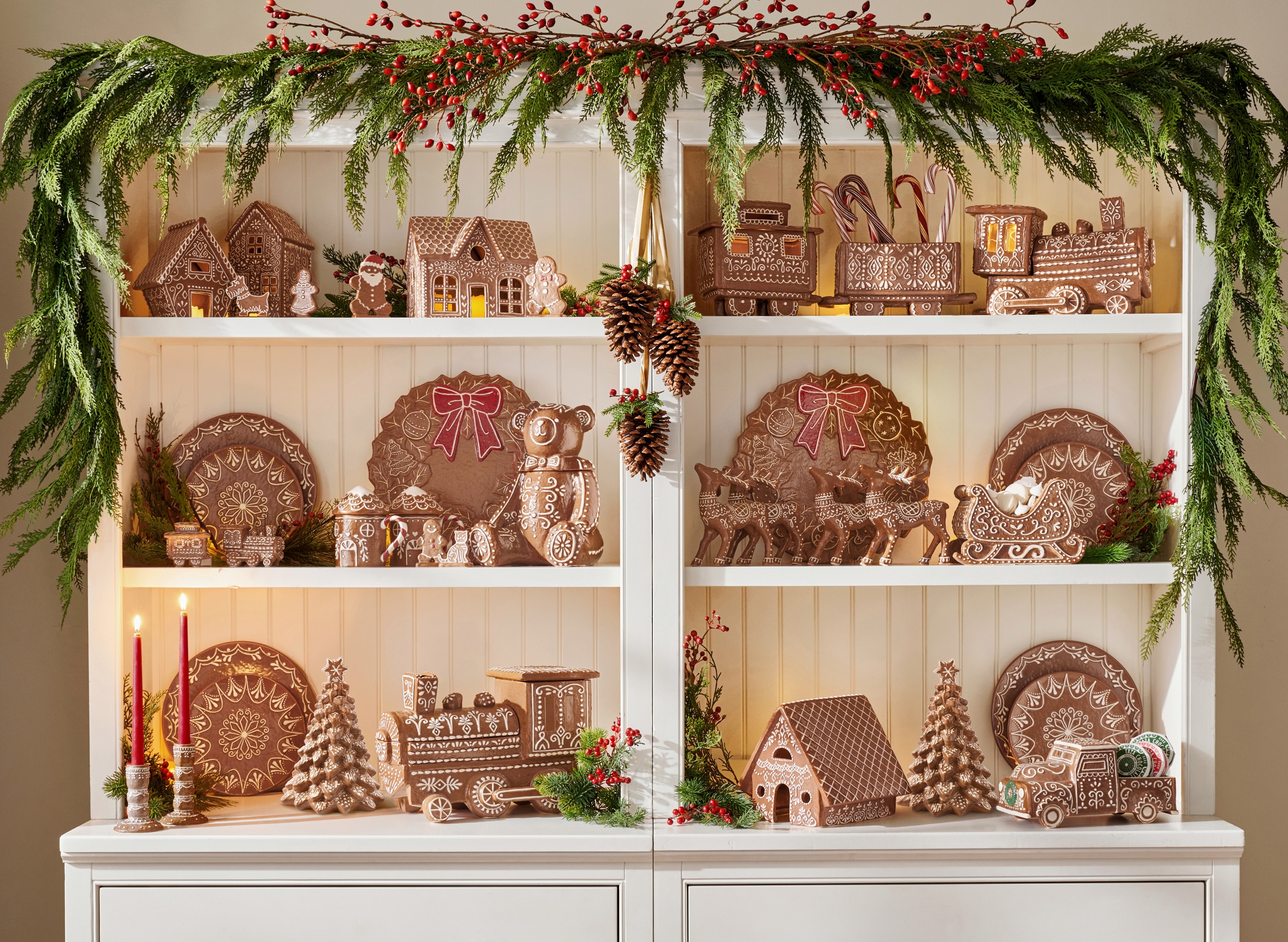 a dresser filled with ceramic gingerbread christmas decor with a garland draped above