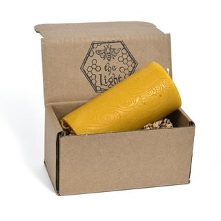  A large yellow pillar candle in a cardboard box. 