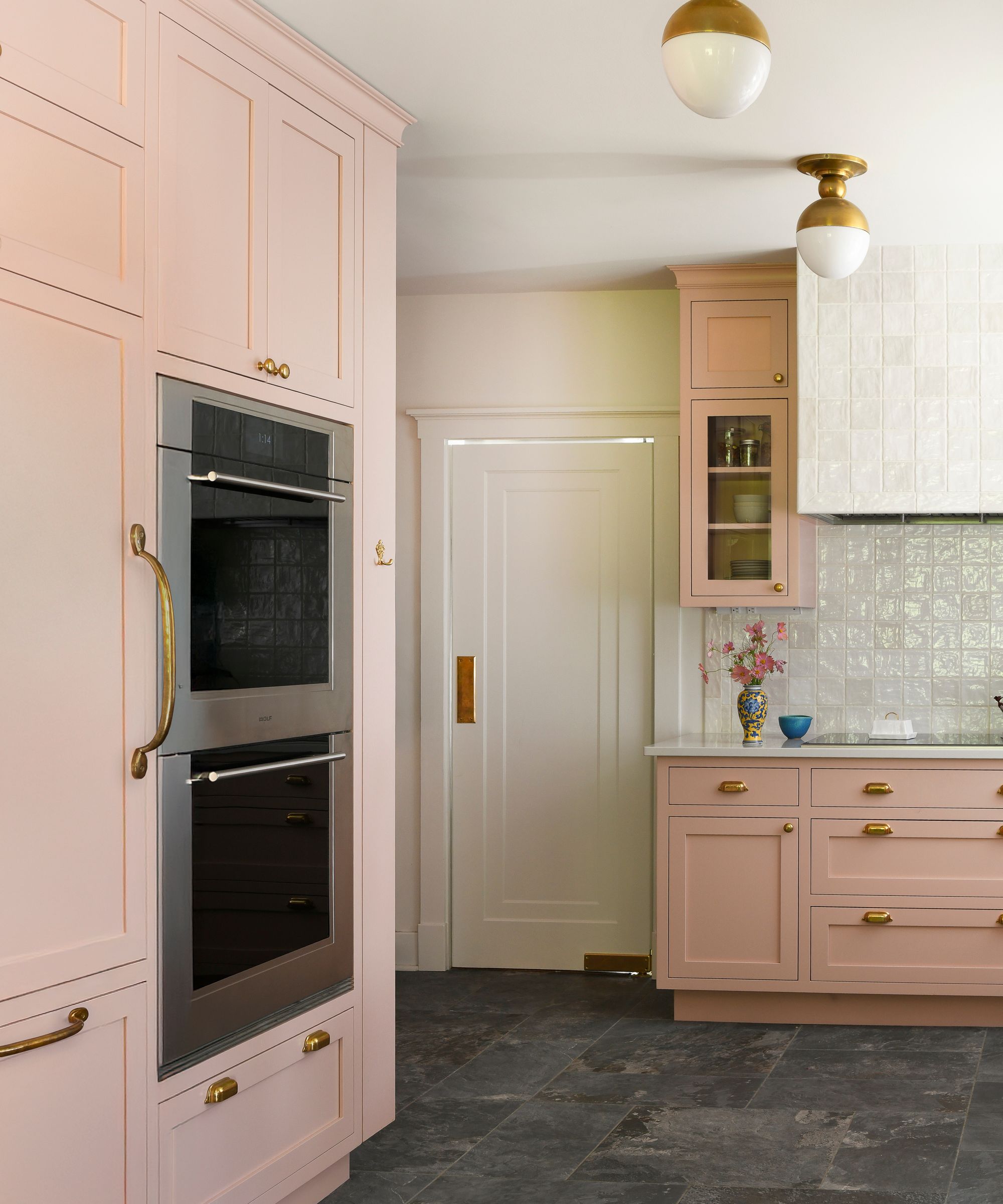 A kitchen with pink cabinets and warm white walls and gray tiled flooring.