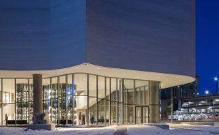 Night time image of the Quamajuq inuit art centre, exterior looking through the glass front at the lit up building and visitors inside, surrounding area and buildings lit up , clear night sky