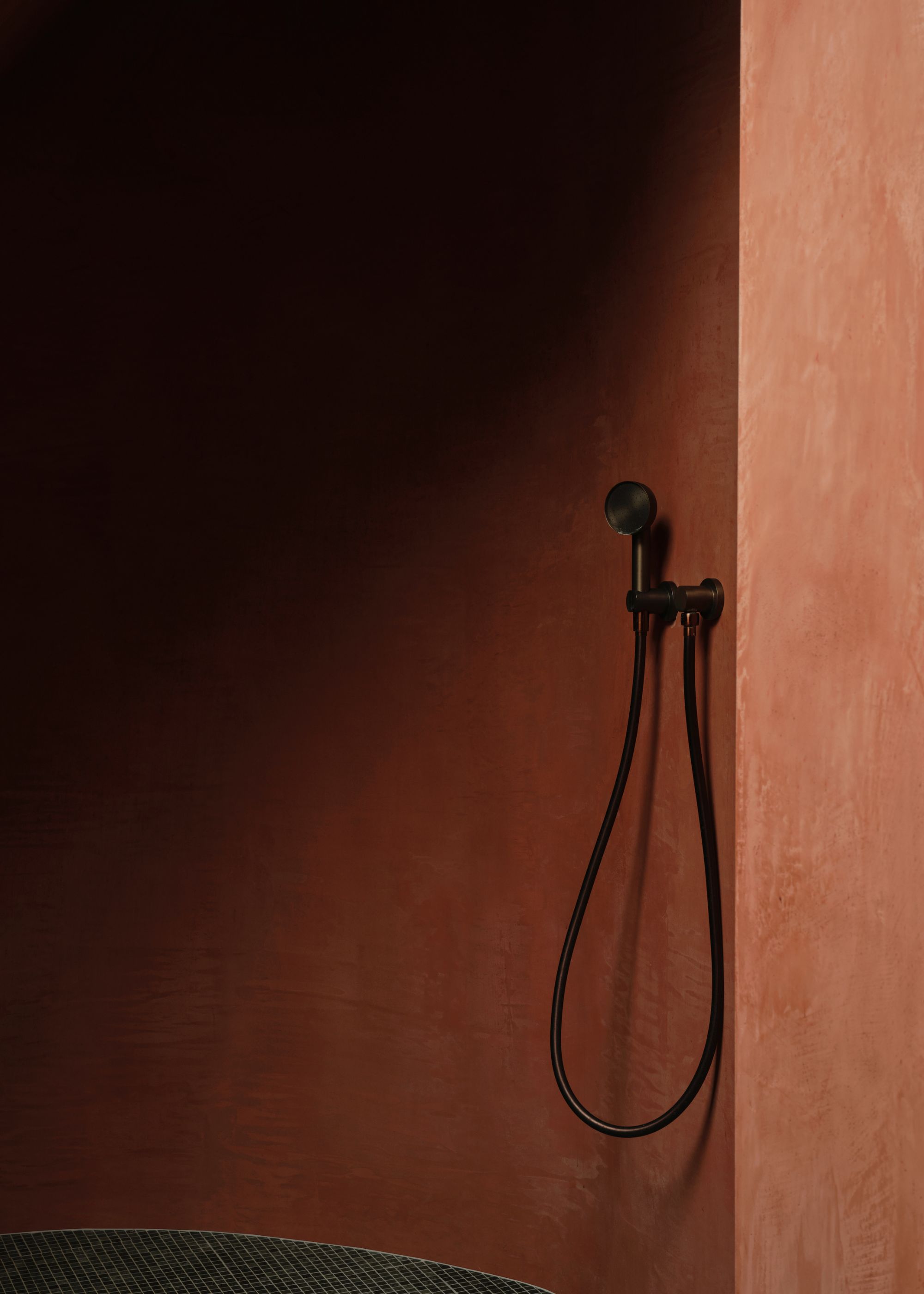 A red colored curved shower with a black shower head feature hanging up.