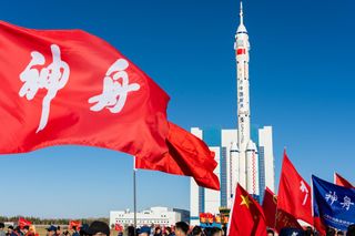 A white rocket with strap on boosters rolls out with a blue sky and Chinese flags.