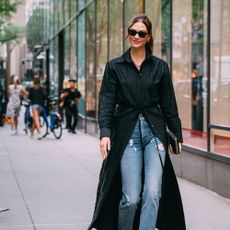 woman wears black maxi top/jacket and jeans while walking on a busy city street