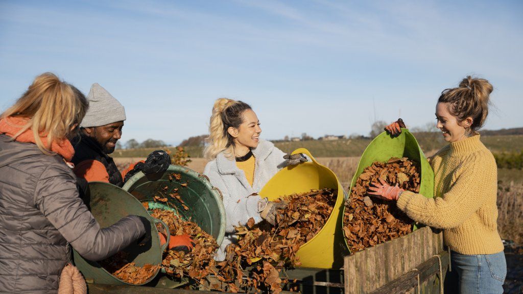 Smiling gardeners add autumn leaves to a compost bin