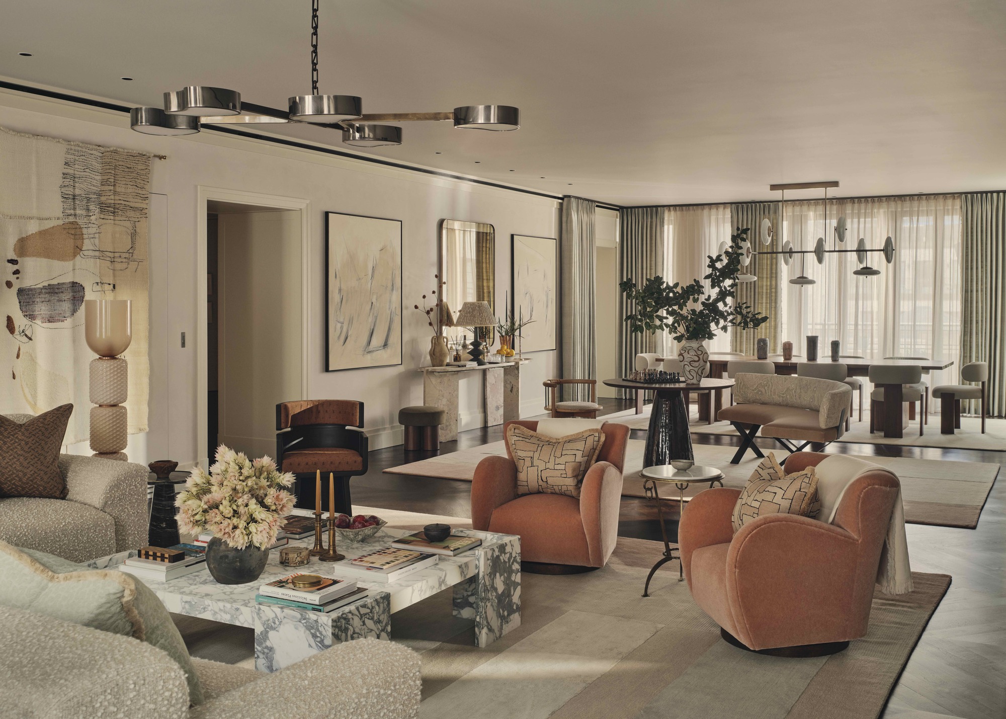 open-plan living and dining room with two orange armchairs pointing towards square marble coffee table styled with lamp, vase of flowers, and coffee table books, and a fuzzy corner sofa