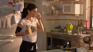 Woman standing in her kitchen eating a banana after exercise, as part of the 5:2 diet plan