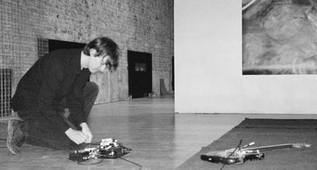 A black-and-white portrait of Bentley Anderson experimenting with a pedalboard as his guitar lies in front of him.