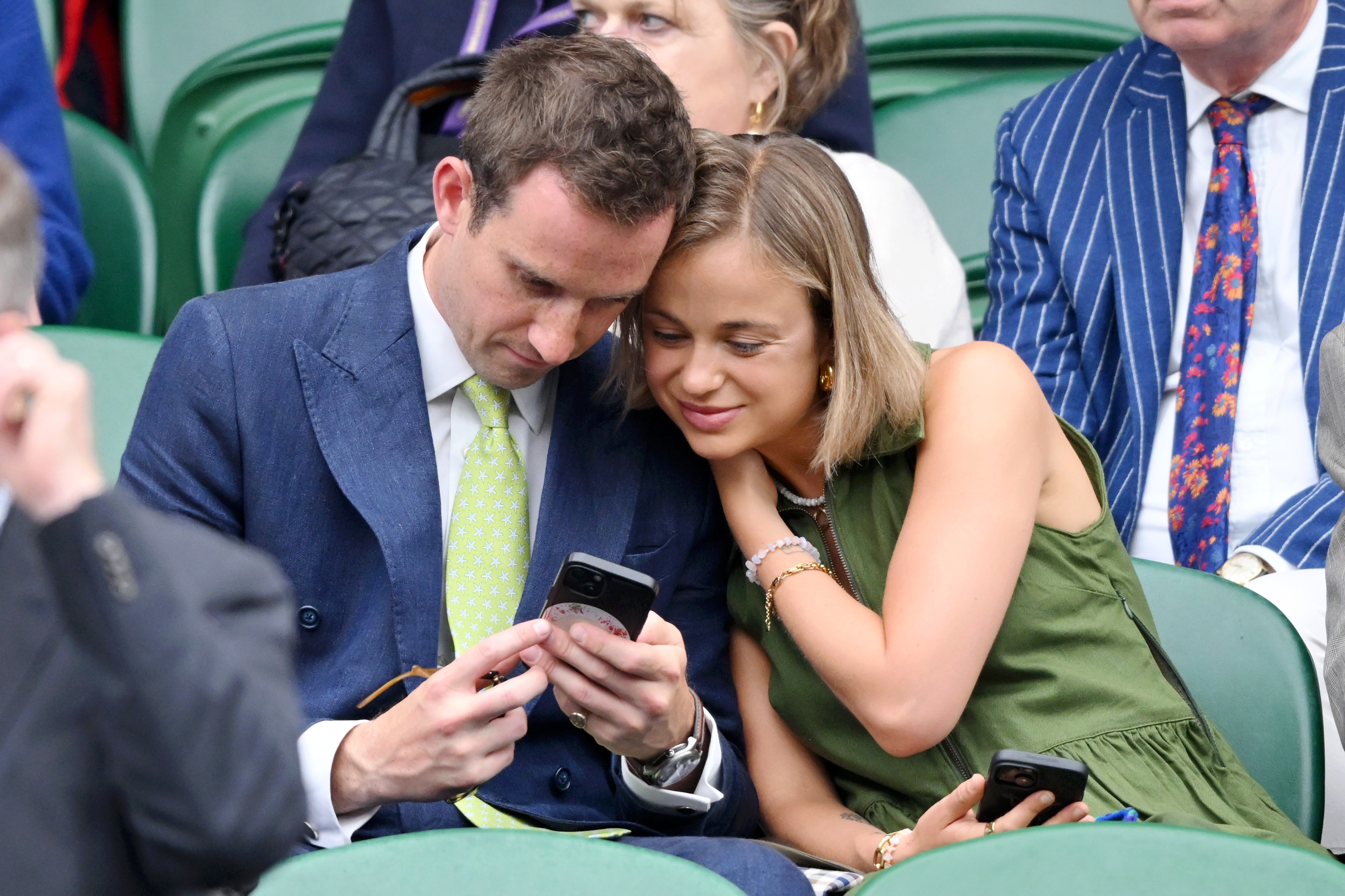 Amelia Windsor and Ollie Lewis looking at a phone during a Wimbledon match