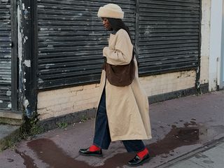 Influencer wears trench coat, jeans, red socks with loafers, hat, and crossbody espresso suede bag.