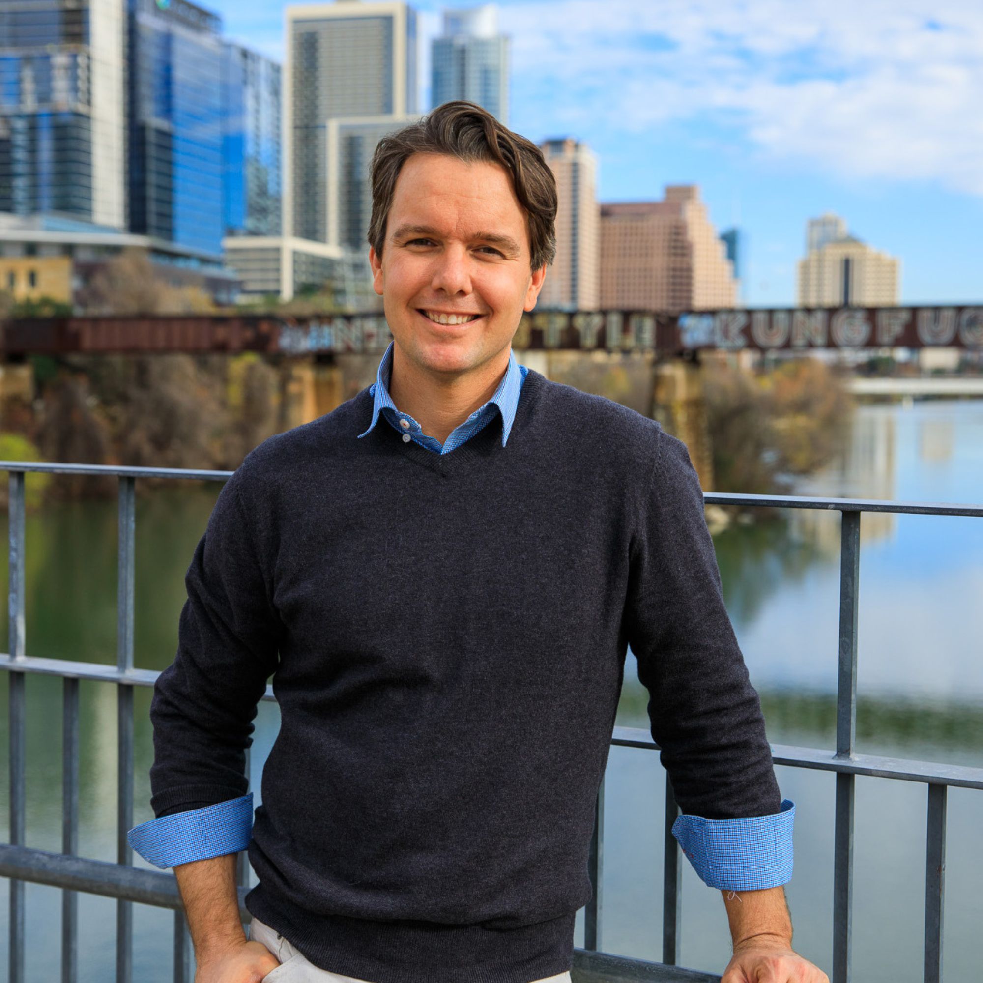 A picture of Eric Bramlett, a man in a blue jumper in front of a river with skyscrapers in the background