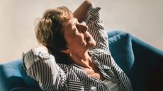 Close-up of an older woman leaning back peacefully in a sunlit room, eyes closed