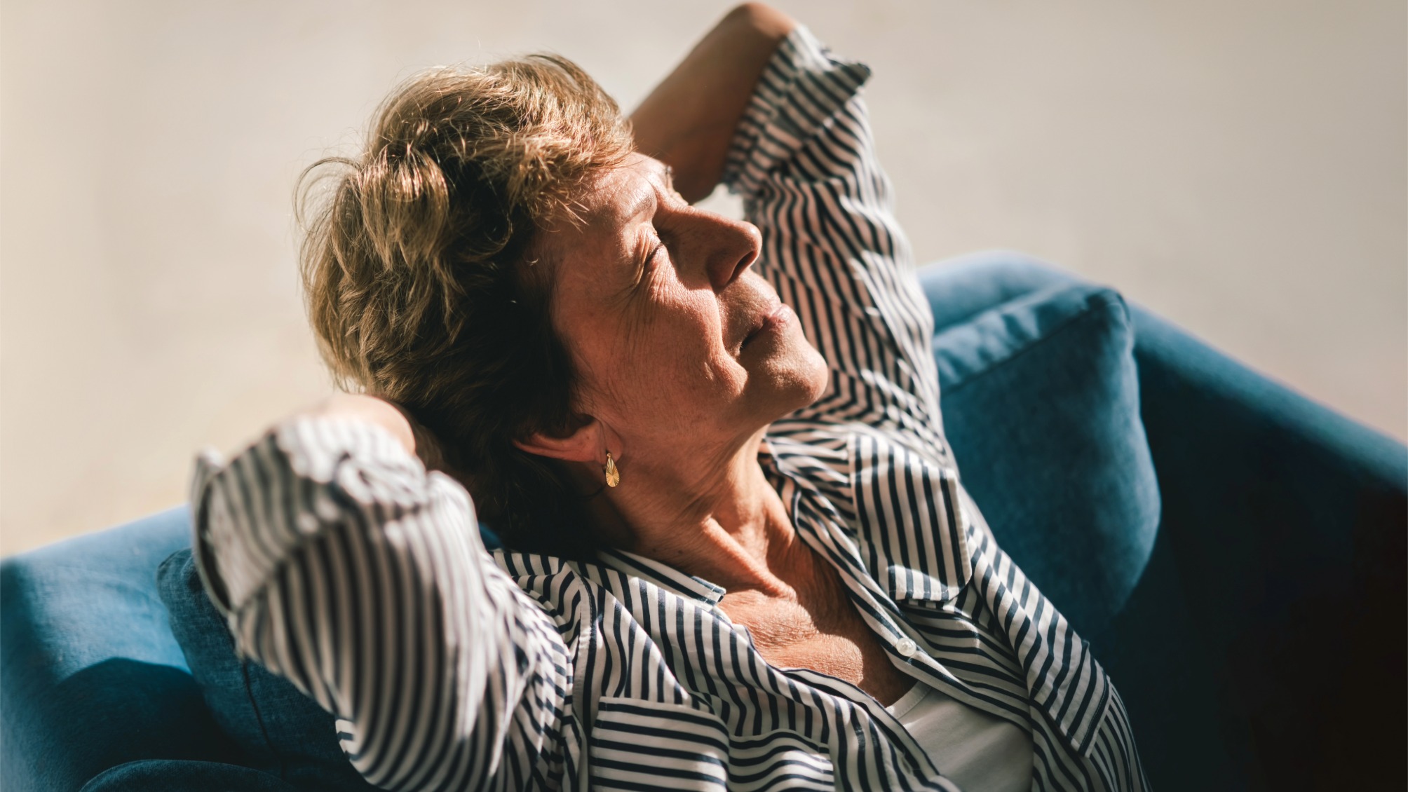 Close-up of an older woman leaning back peacefully in a sunlit room, eyes closed
